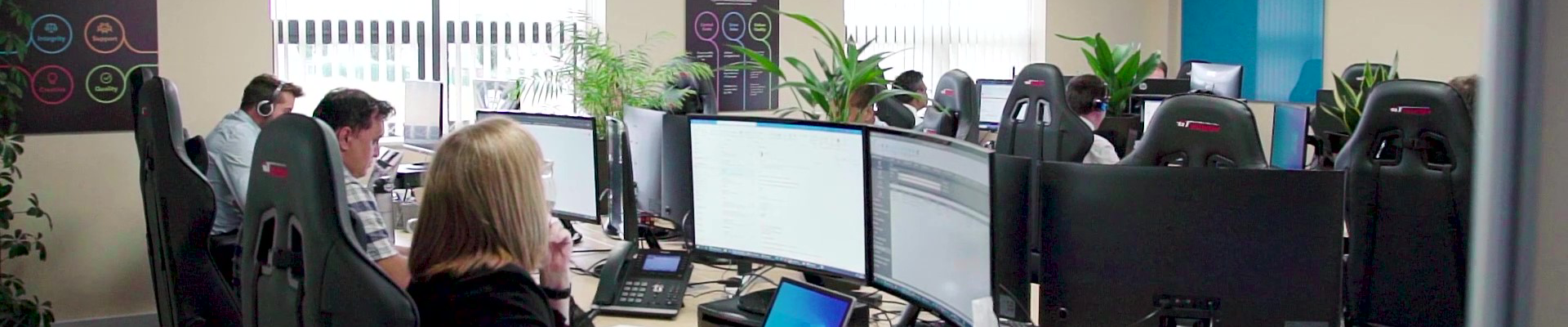 Banner of our software development office with numerous people at desks working