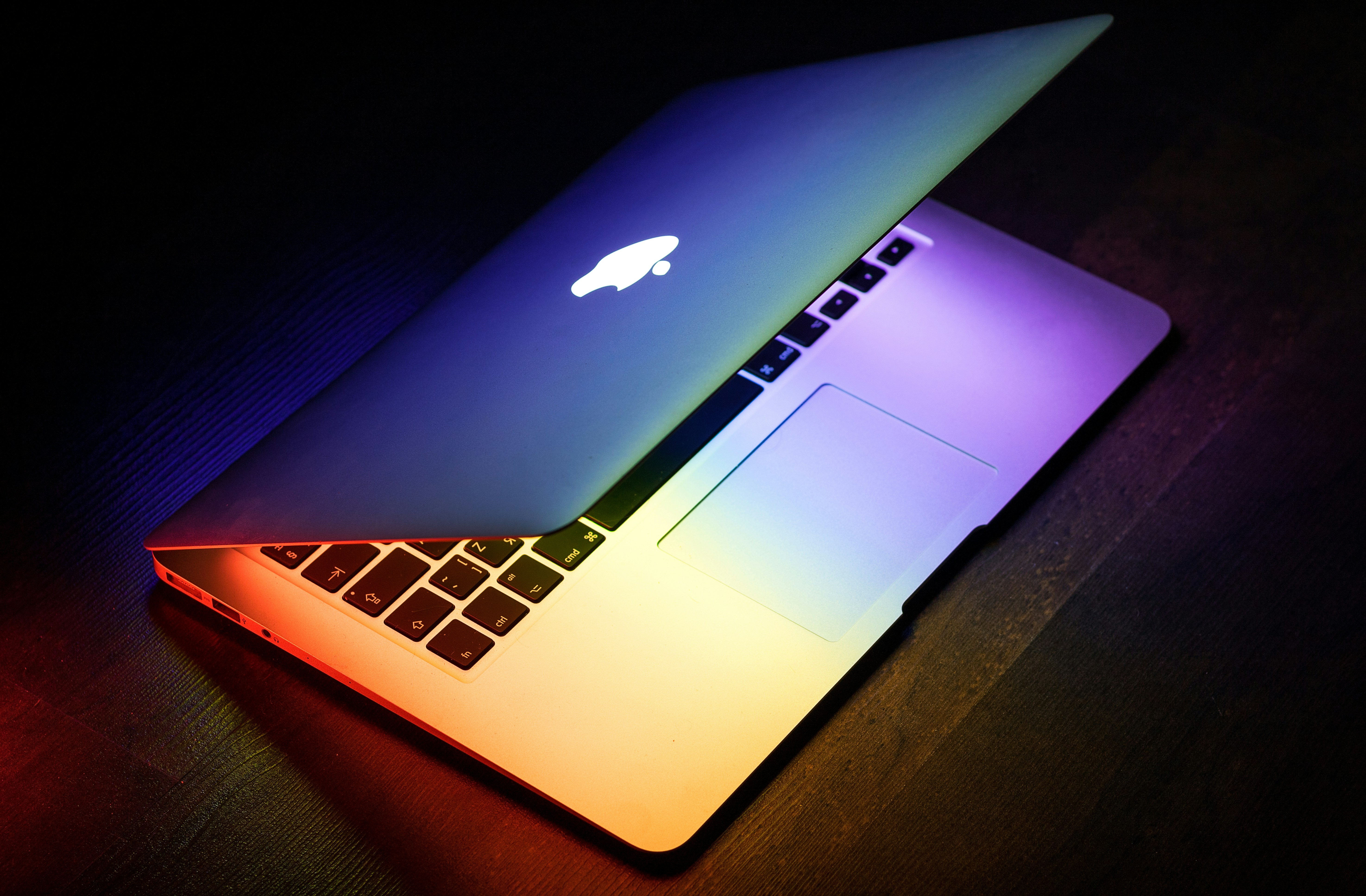 A Macbook pro with the lid half shut and vibrant colours cascading on the desk